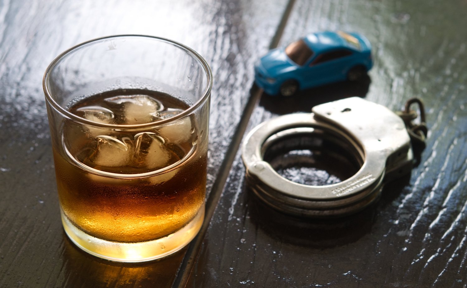 Vaso de licor, un coche de juguete y esposas sobre una mesa de madera