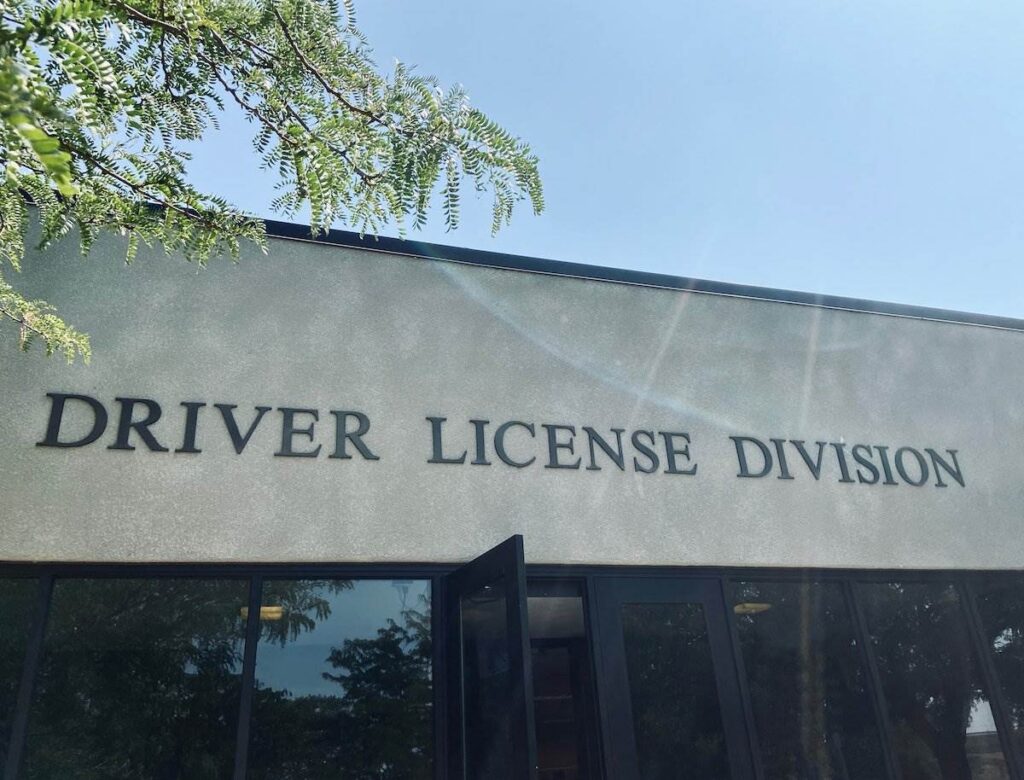Exterior shot of DMV office entrance against blue sky with a tree