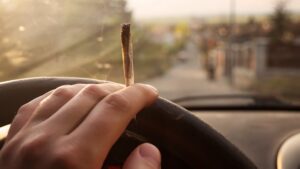 Hand on steering wheel holding a joint during the day