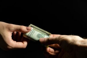 Hand giving cash to another hand againt black background