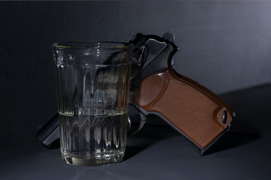 A revolver along with a glass of alcohol against a grey background