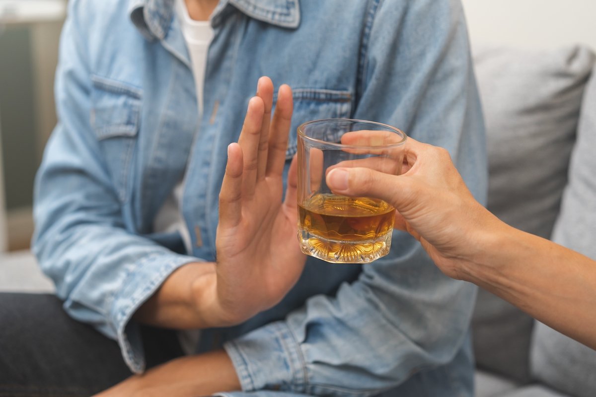 Man putting up his hand rejecting an offer of alcohol by a friend