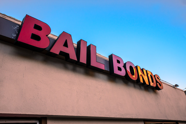 red sign that says "bail bonds"on the storefront of a building, against a blue sky background