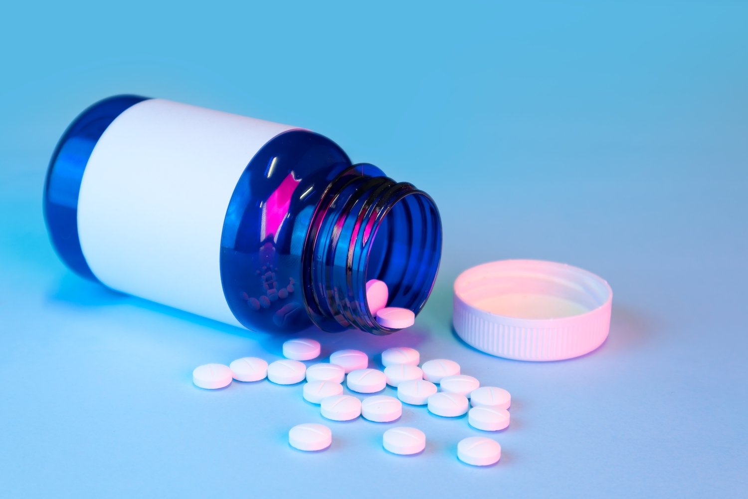open pill bottle on a blue table with pills lying near the bottle