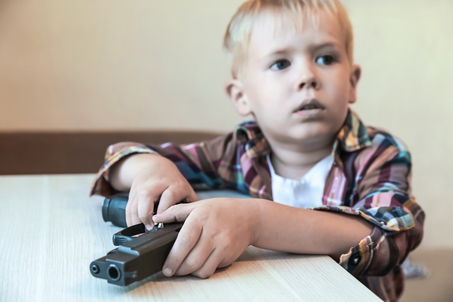 Young boy holding a gun he found on the kitchen table