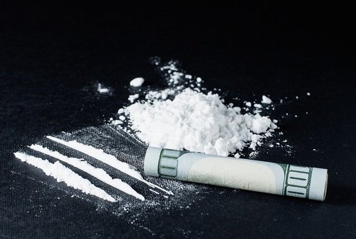 lines of cocaine and a rolled up $100 bill on a black table