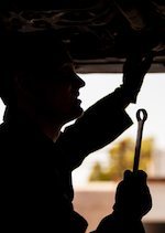 Silhouette of a mechanic working on the underside of a car