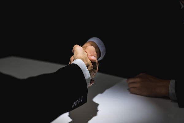 Two people shaking hands in the shadows after conspiring to break the law