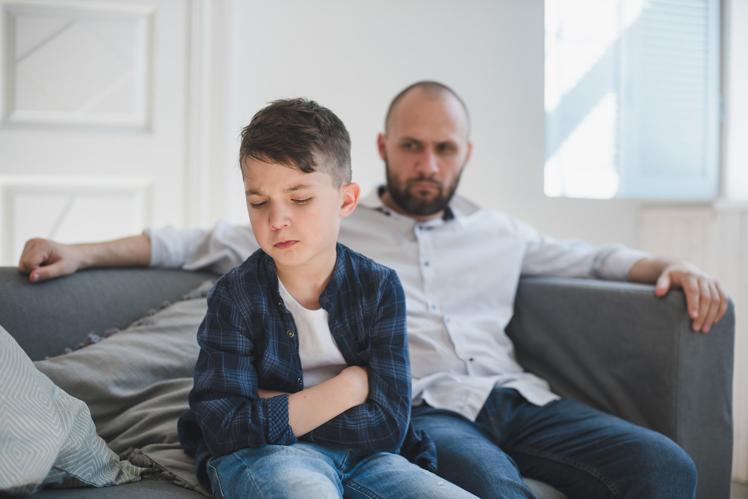 Angry father looking at his young son on a couch in the living room