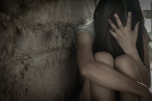 Young trafficked child looking sad by cement wall