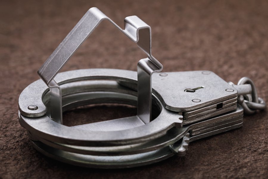 Closeup of handcuffs with a cookie cutter of a house in the cuffs