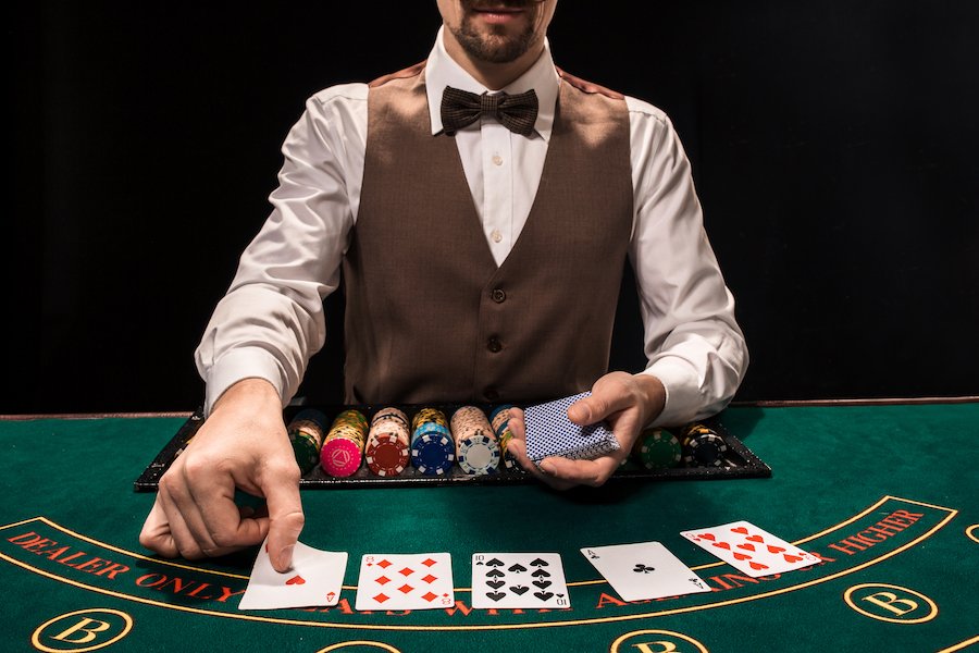 Poker dealer dealing cards on a green felt table with gambling chips by him