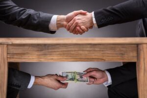 Hands shaking over the table with other hands exchanging money under the table
