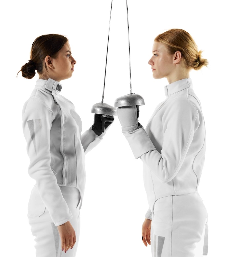 Two females before a fencing match holding foils against a white background