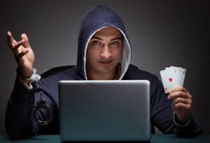 Man in hoodie holding cards in front of a laptop