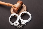 a judge's gavel resting next to a pair of handcuffs on a black table
