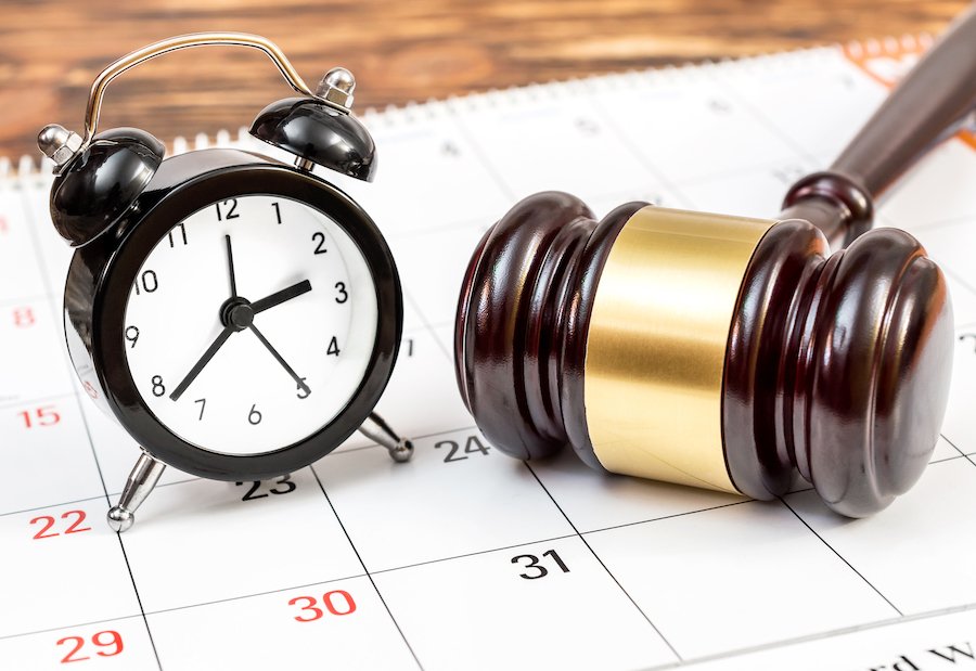 Judge's wooden gavel lying on a calendar next to an alarm clock