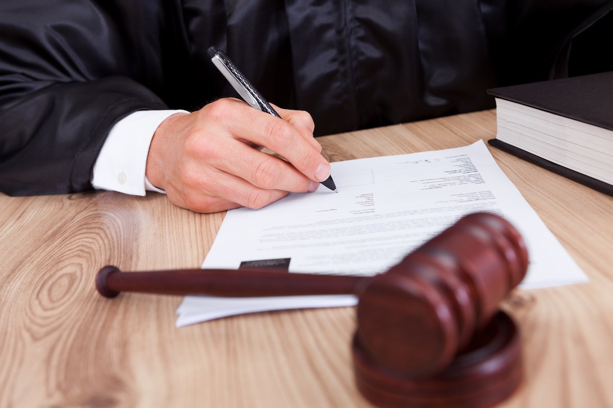 Closeup of a judge's hand signing an order with a gavel in the foreground