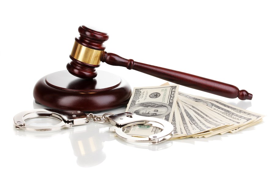 Judge's wooden and gold gavel, silver handcuffs, and thousands in cash bail against a white background
