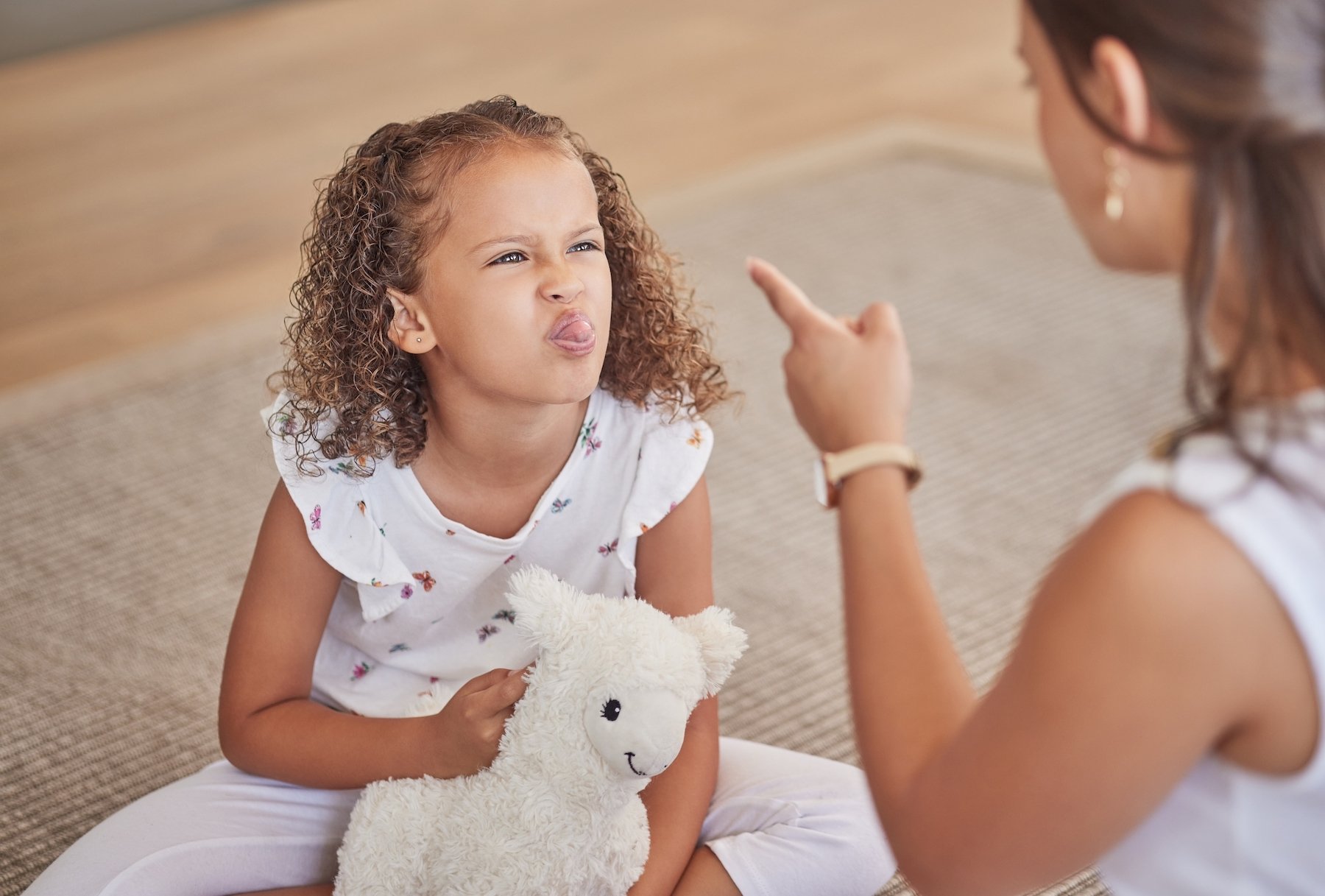 Mother disciplining her child who is sticking her tongue out at her
