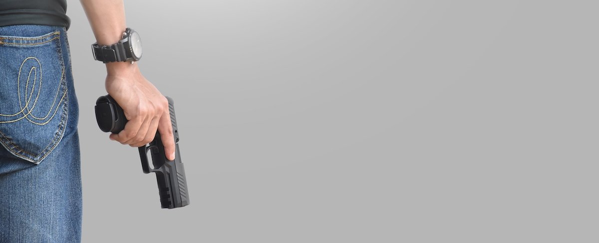 Man in jeans holding a revolver against a grey background