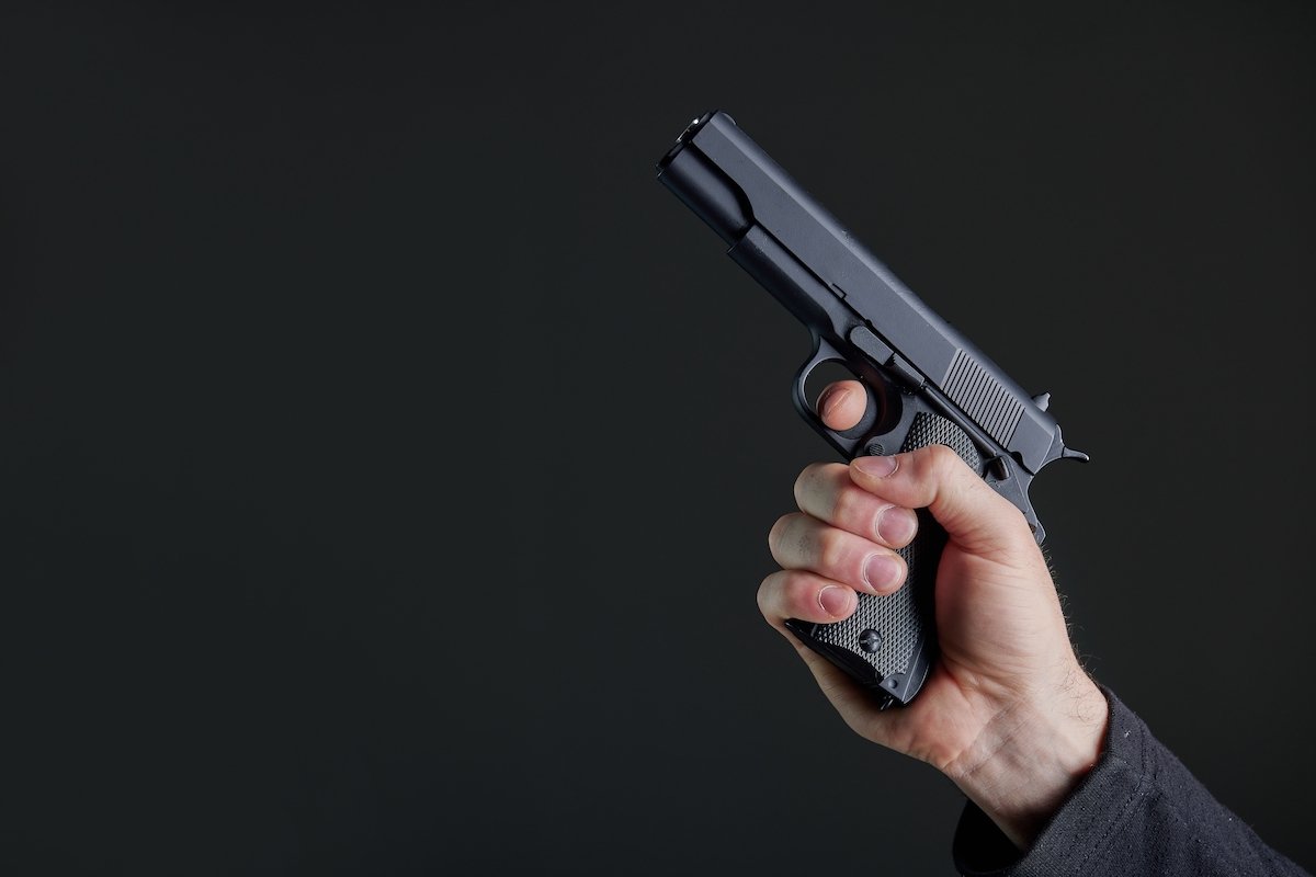 Man holding a gun into the air against a black wall