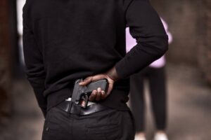 Man in a dark alley about to take out a gun in a prelude to an assault with a deadly weapon
