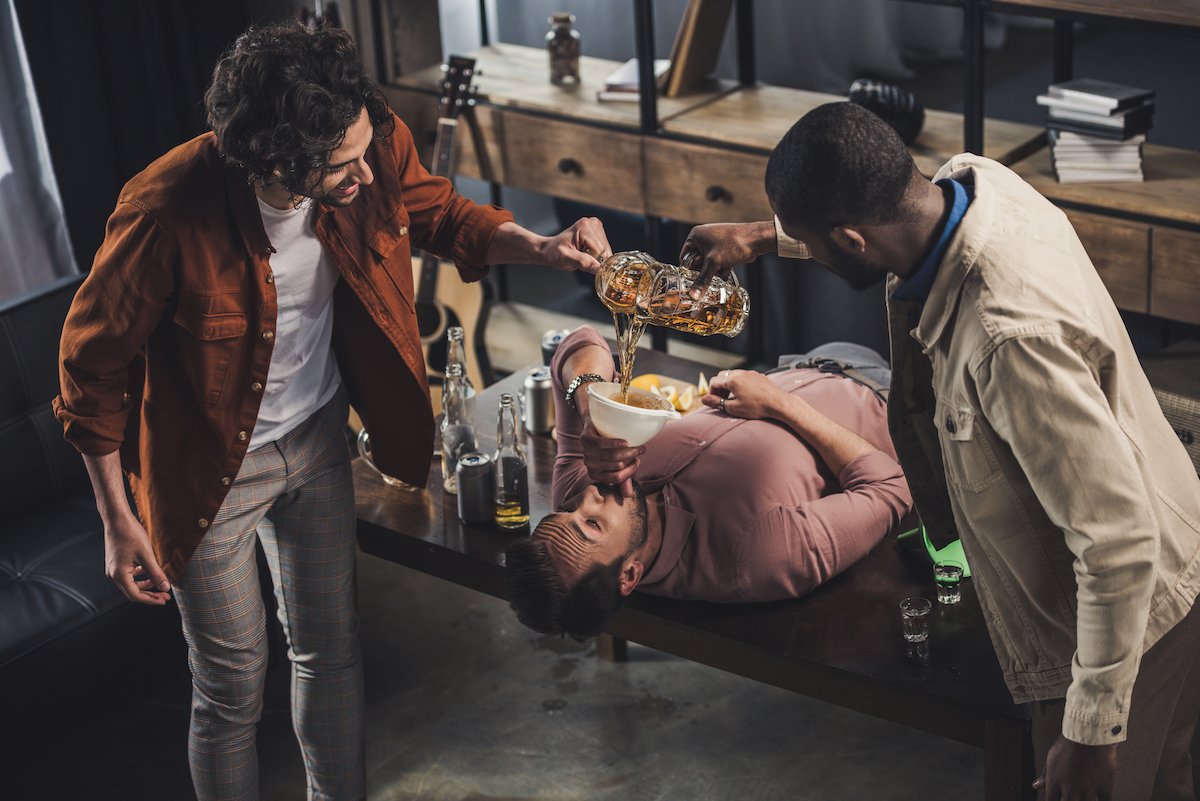 Three college students engaging in hazing by forcing beer consumption. 
