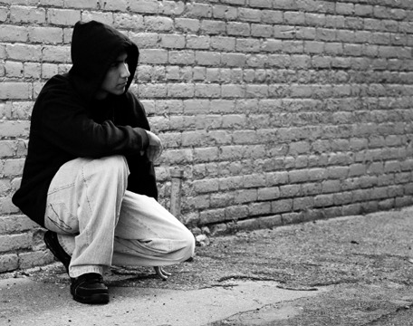 young person in hoodie kneeling against brick wall