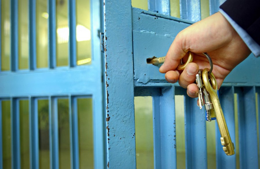 Close-up of police officer hand unlocking the blue door in a prison corridor to let an inmate out on bail