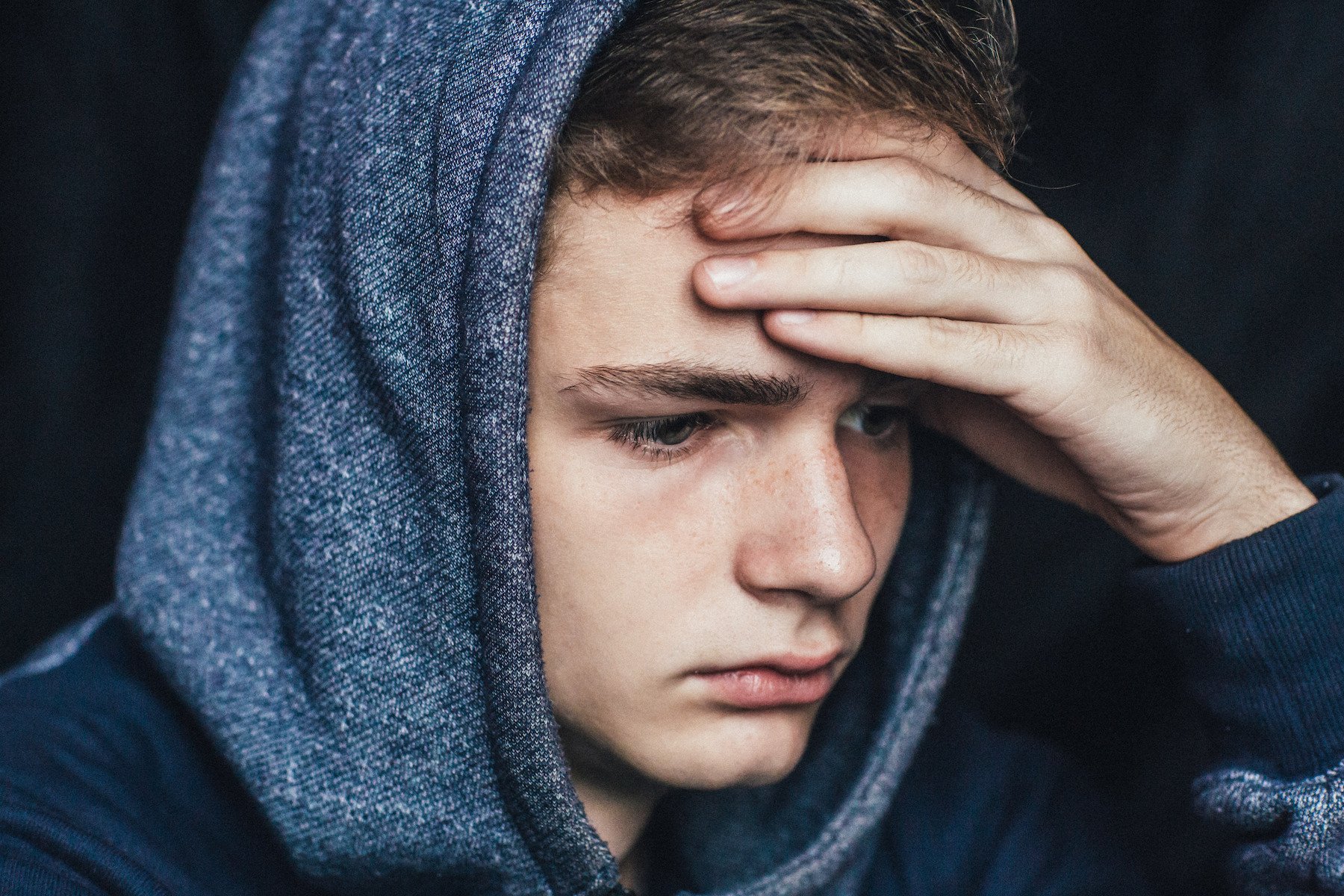 Troubled boy in a hoodie holding his head after being arrested