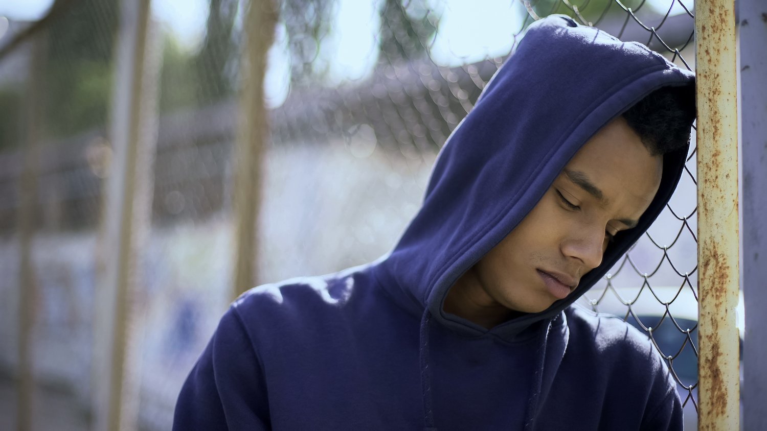 Boy in a hoodie leaning against the gate at juvenile detention