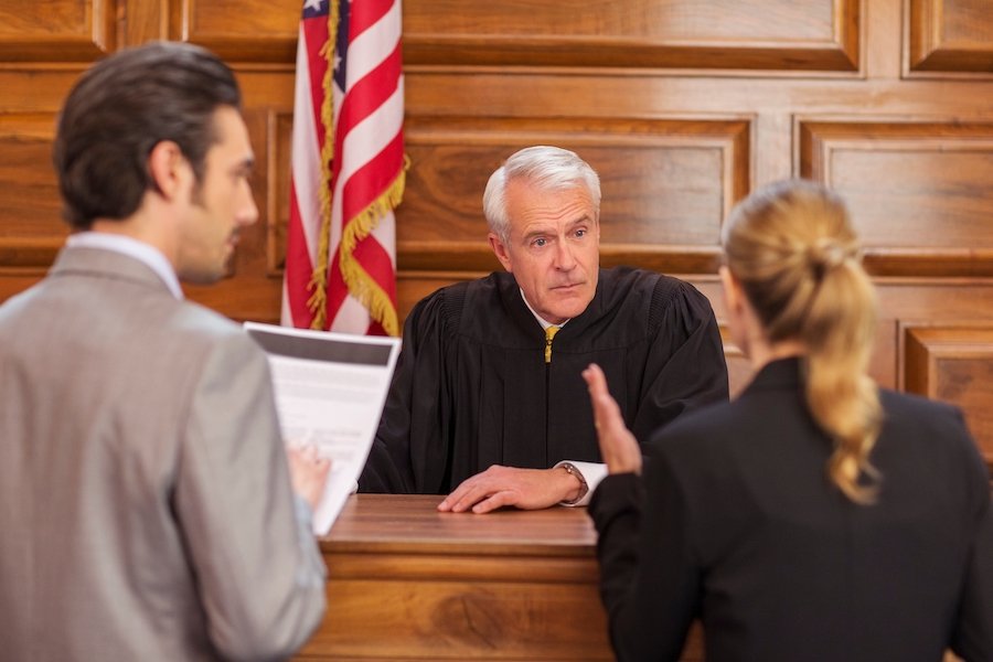 Two attorneys speaking with a judge at the bench with a flag behind him