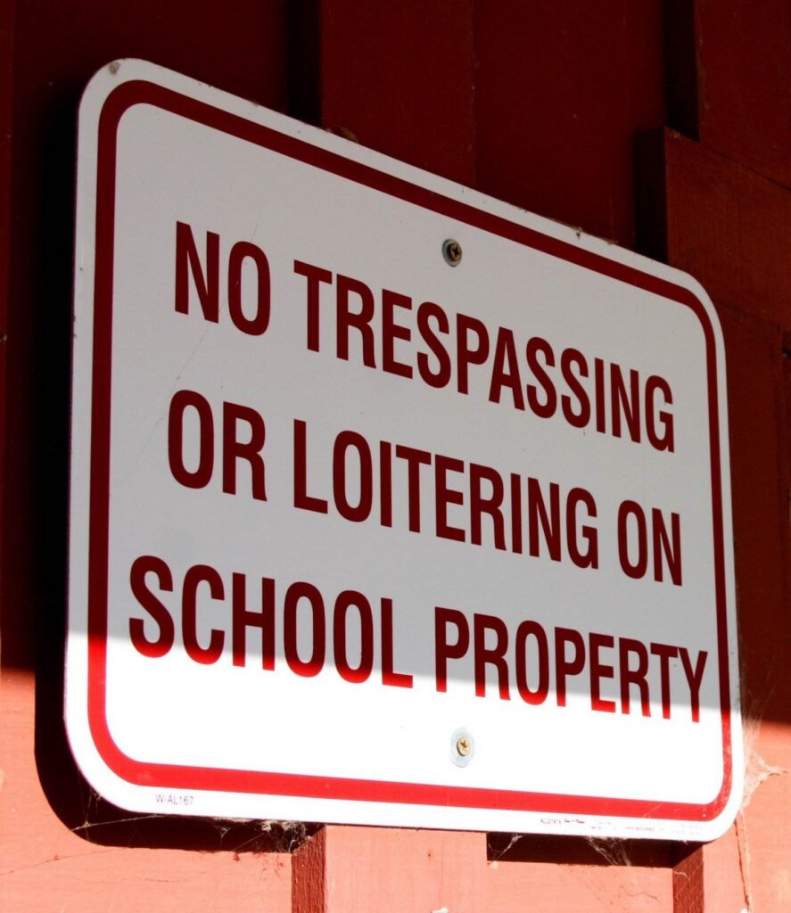 Red and white sign that says, "No Trespassing or Loitering on School Property" posted on a red wall