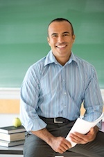 teacher sitting on desk with papers in hand