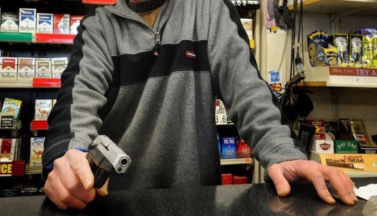 man holding a gun at the cashier's desk about to commit robbery in a bodega