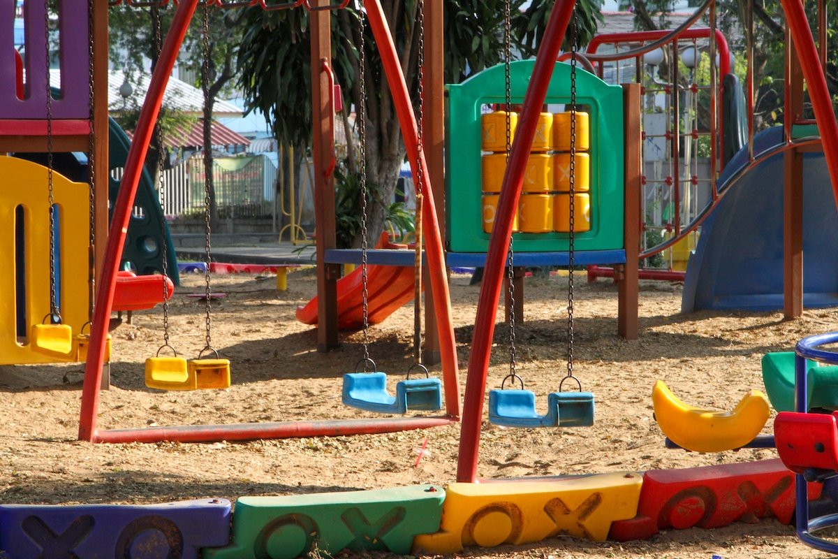 An empty children's playground with swings and trees