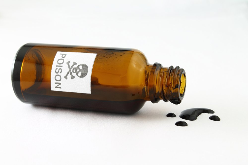 An overturned vial of poison with a skull and crossbones label on it and some of the liquid poison dripping on the table, against a white background