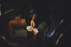 John handing cash to prostitute in the front seat of a sedan at night