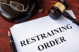 Paper that says "restraining order" with a gavel, pen, and judge's glasses