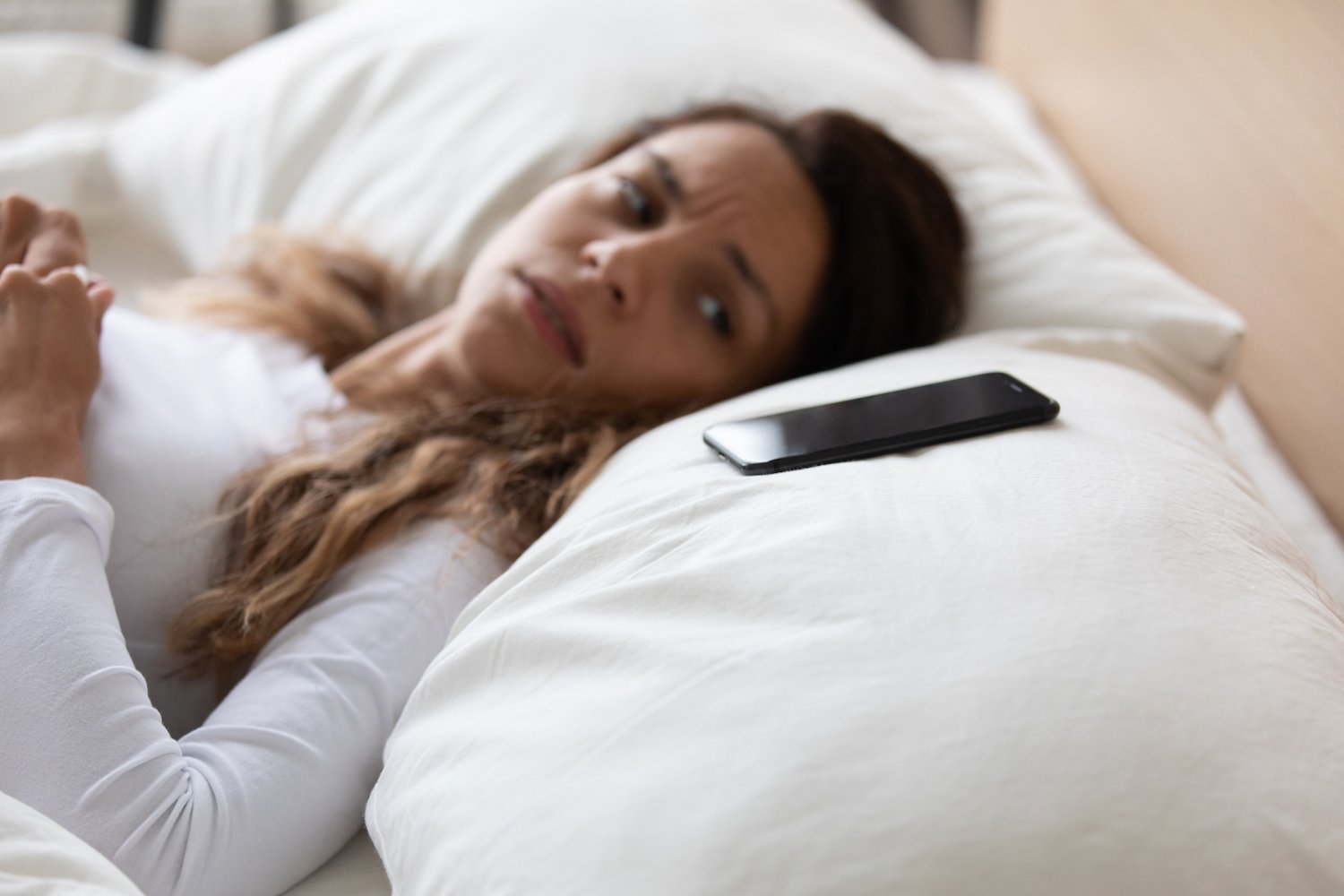 Scared woman lying on pillow looking at her phone