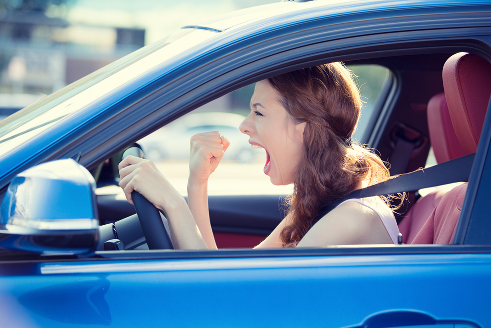 Red-haired woman in blue car screaming in frustration with one fist raised