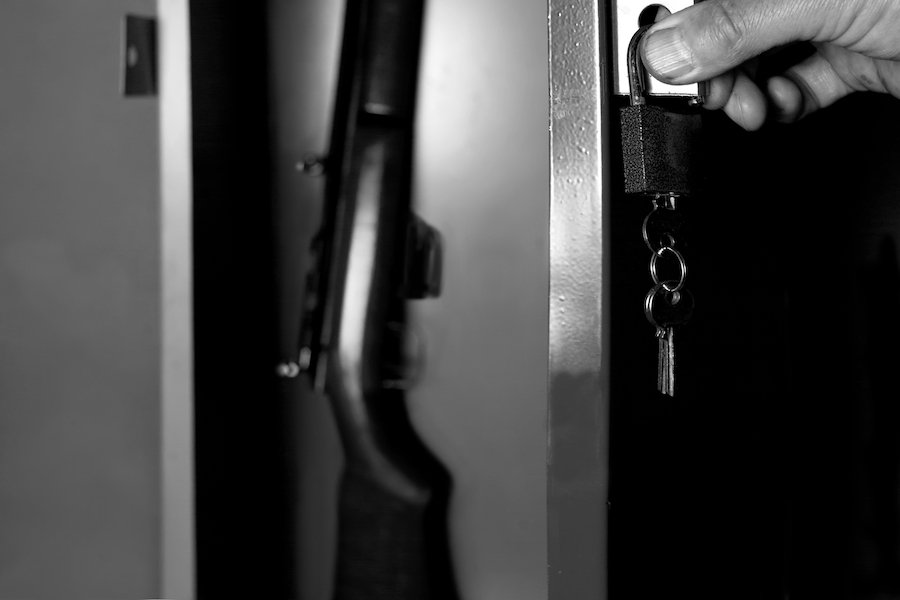 Black and white photo of a human hand opening a gun cabinet holding a rifle