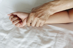 male hand holding down woman's hand in bed