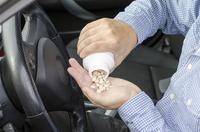 Motorist in driver's seat pouring bottle of pills into his hand to illustrate DUI of prescription painkillers in Nevada