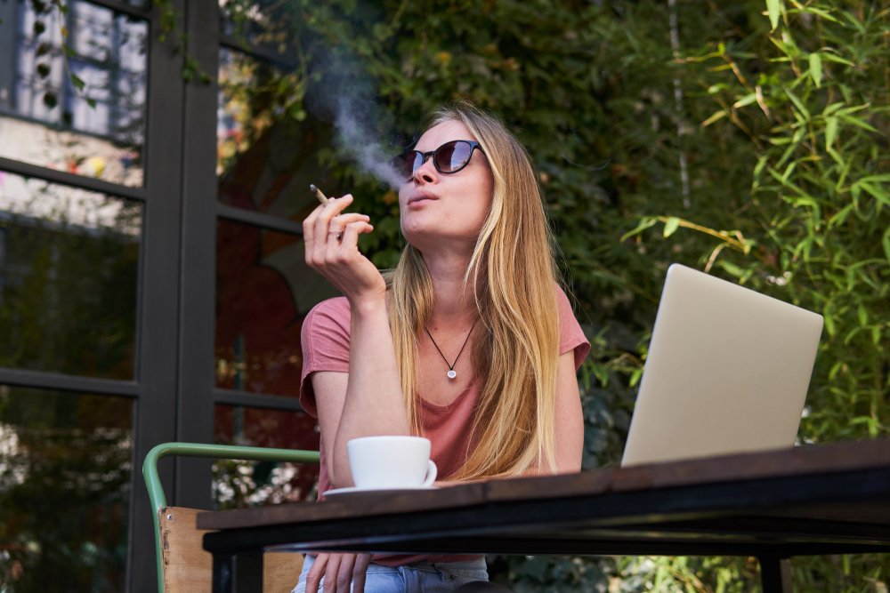 A woman smoking marijuana outdoors while sitting at a cafe.