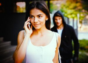 Man in hoodie stalking young lady on her phone on the street