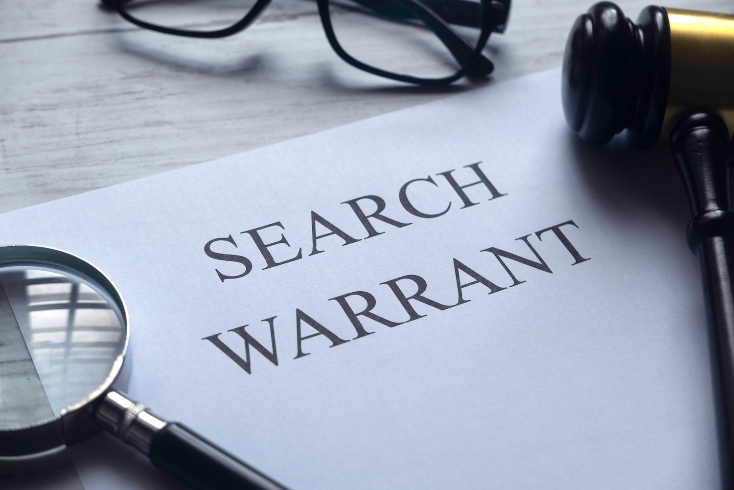 Paper that says "search warrant" next to a gavel, pen, and glasses