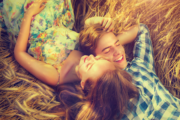 A bird's eye shot of a smiling young man and smiling young woman lying on a bed of golden straw canoodling