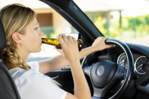 Woman driver drinking a beer she is holding with one hand while her other hand is on the wheel steering